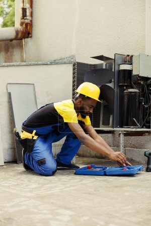 Photo for Adept african american repairman starting routine maintenance on external hvac system, preparing toolbox. Technician getting tools ready for checking faulty air conditioner internal parts - Royalty Free Image
