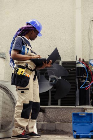 Photo for Expert commissioned for yearly professional maintenance to avoid costly fixings and ensure condenser systems longevity. Experienced professional doing hvac unit checkup, imputing data on laptop - Royalty Free Image