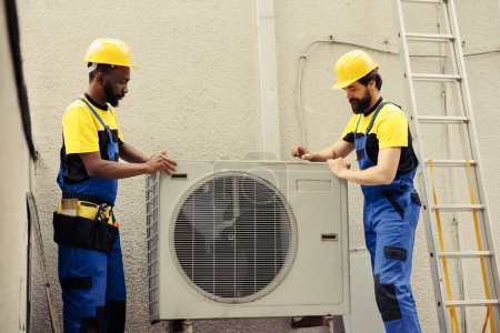 Photo for Teamworking certified technicians starting work on broken hvac system, taking apart condenser coil panel. Expert wiremen disassembling air conditioner to check for bad wiring - Royalty Free Image