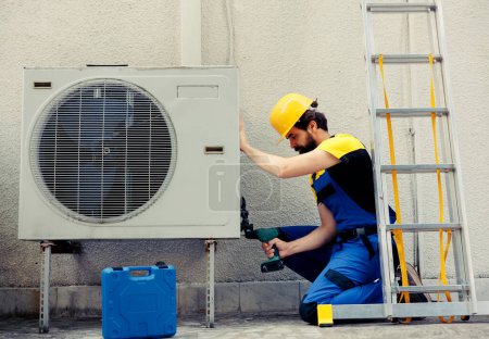 Photo for Competent repairman starting work on defective air conditioner, using handheld drill to disassemble condenser metal coil panel. Precise mechanic dismantling hvac system to check for dirt - Royalty Free Image