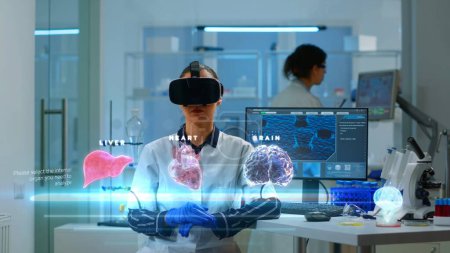 Téléchargez les photos : Femme scientifique dans une clinique moderne portant un casque VR, utilisant un équipement de pointe et des capteurs filaires pour contribuer à la recherche en neurologie, améliorer la compréhension des organes humains - en image libre de droit