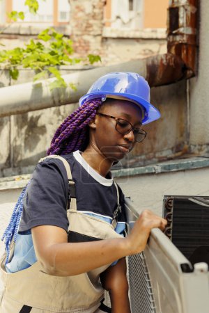 Téléchargez les photos : Spécialiste afro-américain assemblant à nouveau climatiseur après avoir fini de reconditionner les composants rouillés. Ingénieur agréé comissionné par le client pour effectuer la maintenance sur le système hvac - en image libre de droit