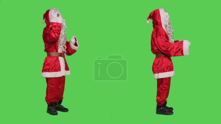 Foto de Santa Claus peleando con la gente, discutiendo sobre la pantalla verde de cuerpo entero. Joven adulto retratando la Navidad del padre en traje rojo estacional, conflicto durante el evento de vacaciones de invierno. - Imagen libre de derechos