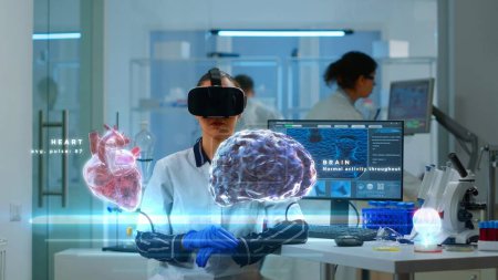 Téléchargez les photos : Expert scientifique en laboratoire moderne portant un casque VR, utilisant des équipements avancés et des capteurs filaires pour contribuer à la recherche en neurologie. Spécialiste utilisant la technologie de réalité virtuelle pour acquérir des connaissances médicales - en image libre de droit