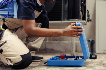 Photo for Adept worker unpacking toolbox with professional equipment needed to repair broken air conditioner blower fan. Certified technician preparing for annual hvac system maintenance - Royalty Free Image