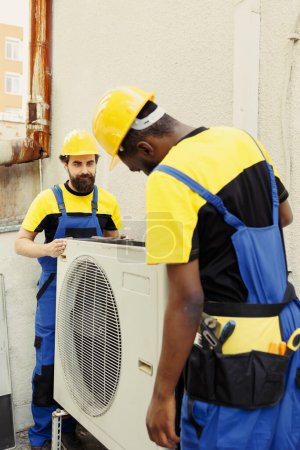 Photo for Precise serviceman and african american colleague installing new external hvac system for client. Meticulous wiremen optimizing new air conditioner performance, ensuring it operates at productivity - Royalty Free Image