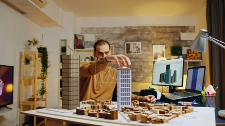 Téléchargez les photos : Architecte modélisant des bâtiments dans le salon de bureau à domicile, suivant des plans de croquis de conception graphique 3D sur l'écran d'ordinateur. Professionnel travaillant sur la maquette de structure de gratte-ciel - en image libre de droit