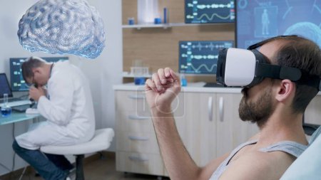 Foto de Experimento sujeto acostado en cama de laboratorio con auriculares de realidad virtual, ver visualización holográfica de la mente AR mientras el científico monitorea la actividad cerebral, contribuyendo al desarrollo del campo de neurología - Imagen libre de derechos