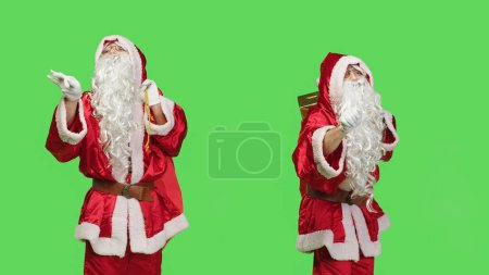 Téléchargez les photos : Santa chef d'orchestre musique pour orchestre à jouer pendant les fêtes de fin d'année, accompagner le groupe sur écran vert. Musicien en chef en costume rouge agissant comme un chef d'orchestre, Noël. - en image libre de droit
