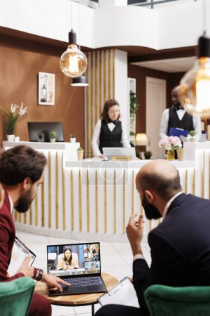 Téléchargez les photos : Les hommes d'affaires parlent sur vidéocall en ligne, se réunissent dans le salon de l'hôtel pour appeler les employés par vidéoconférence à distance. Professionnels participant à la téléconférence en ligne, nouveau partenariat. - en image libre de droit