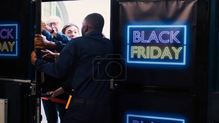 Photo for Security guard keeping people in check before opening clothing store on black friday. Crazy mad diverse shoppers standing behind red tape at shopping center entrance during sales. - Royalty Free Image