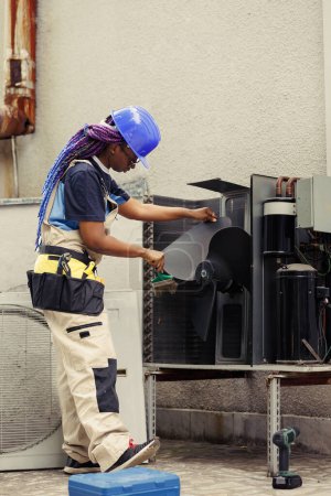 Téléchargez les photos : Technicien certifié afro-américain nettoyage couche accumulée de saleté et de poussière des pièces internes du climatiseur pour empêcher la réduction de la capacité de refroidissement et de la capacité de travail - en image libre de droit