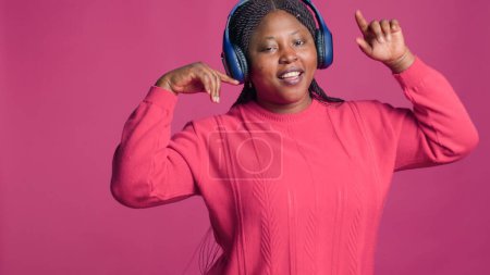 Foto de Mujer negra alegre con auriculares modernos moviéndose y pasándola bien. Dama con etnia afroamericana bailando con confianza con buena música desde auriculares estéreo. - Imagen libre de derechos