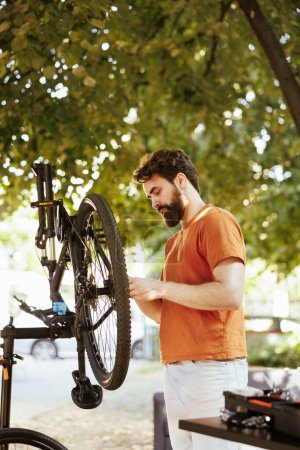 Photo for Young enthusiastic caucasian man outside doing yearly upkeeping and maintenance of modern bicycle. Healthy male cyclist seen outdoors checking bike for damages to repair and adjust. - Royalty Free Image