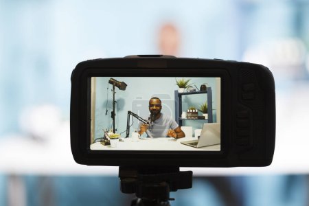 Téléchargez les photos : Blogger en direct en streaming sur le blog en ligne en utilisant la caméra professionnelle gros plan. Vidéo d'enregistrement de vlogger afro-américain souriant avec équipement de vidéographie et parlant au microphone - en image libre de droit