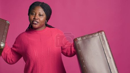 Photo for Female african american traveler confidently showcasing stylish brown suitcases. Beautiful black woman with vibrant smile standing with two pieces of luggage ready to travel in fashion. - Royalty Free Image