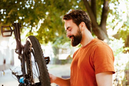 Photo for Active determined male cyclist confidently repairing bike rim and inspecting tire for outdoor leisure cycling. Dedicated sports-loving man performing bike maintenance essential work tool. - Royalty Free Image