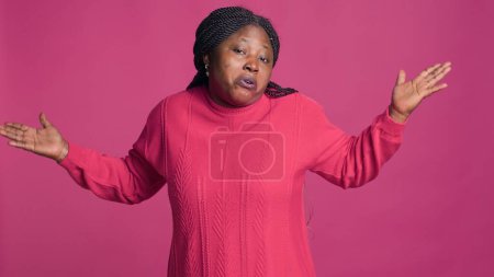 Photo for Female fashion blogger standing and looking at camera with baffled expression. Youthful black woman with her hands out motioning no idea no clue illustration against isolated pink background. - Royalty Free Image