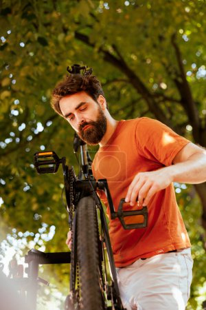 Photo for Detailed image of energetic caucasian man precisely fixing and fastening crank arm and pedal on bicycle. Male cyclist performing annual maintenance on bike parts in yard, close-up. - Royalty Free Image