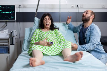 Photo for Young couple preparing to be parents in hospital ward bed at healthcare facility. Pregnant woman having painful contractions getting into labor while husband asking for medical assistance - Royalty Free Image