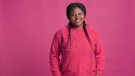 Foto de Elegante mujer afroamericana posando en un suéter rosa vibrante para una foto impresionante. Retrato de una joven mujer negra con un atuendo de moda sonriendo a la cámara para una foto. - Imagen libre de derechos