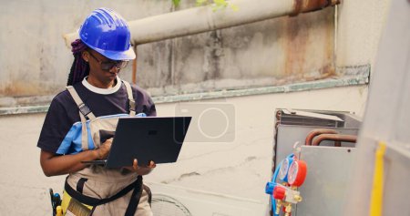 Photo for Experienced engineer working on external hvac system, holding laptop. Meticulous wireman optimizing outdoor condenser performance, ensuring it operates at maximum capacity - Royalty Free Image