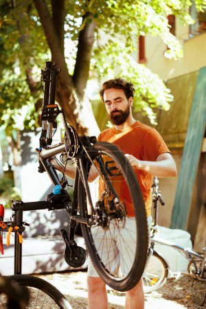 Photo for Image showcasing committed healthy athletic man meticulously inspecting modern bicycle for regular summer maintenance. Active young caucasian male carefully grasping bike components for repair. - Royalty Free Image