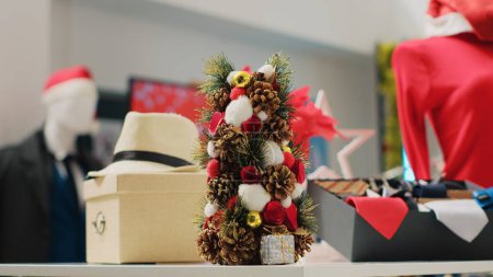 Téléchargez les photos : Gros plan des décorations de Noël festives dans le magasin de vêtements pendant la saison des fêtes d'hiver. Affichage d'ornements de Noël, guirlandes et vêtements de vêtements formels dans la boutique de mode - en image libre de droit