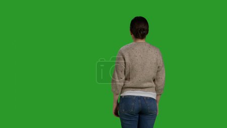 Foto de Back view of person showing denial and pushing something aside, expressing refusal and rejection looking displeased. Female model acting discontent and moving object, standing over greenscreen. - Imagen libre de derechos