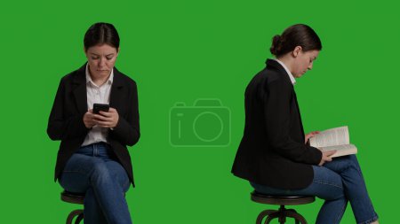 Photo for Close up of manager reading book and texting messages on camera, sitting on chair. Employee focusing on novel chapter to read tale, enjoying story and wearing suit over greenscreen backdrop. - Royalty Free Image