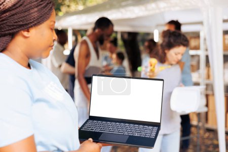 Photo for Close-up image showcasing african american female charity worker handling a laptop with blank mockup template. Black woman grasps a minicomputer with isolated copyspace white screen for customization. - Royalty Free Image