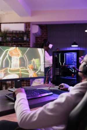 Photo for Man in brick wall living room playing entertaining video games on gaming PC at computer desk, resting after work. Gamer competing against enemies in internet multiplayer shooter - Royalty Free Image