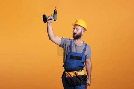 Photo for Young carpenter working wtih electric power drill tool, wearing overalls and holding drilling gun. Handyman contractor using cordless drill to work on renovation and refurbishment. - Royalty Free Image