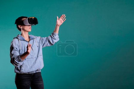 Photo for Cheerful woman wearing virtual reality headset in 3d simulation using interactive equippment. Female adult with vr goggles having futuristic experience with videogame using modern digital technology. - Royalty Free Image
