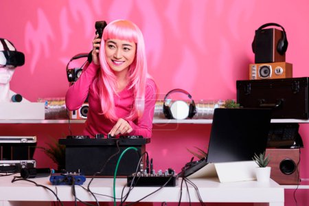 Téléchargez les photos : Artiste aux cheveux roses mélangeant chanson techno sur des platines professionnelles écoutant de la musique avec casque tout en faisant des performances en club pendant la nuit. Album d'enregistrement de femmes utilisant du matériel audio - en image libre de droit