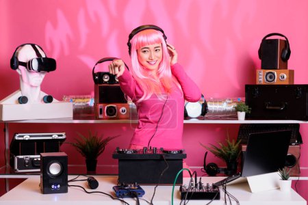 Téléchargez les photos : Musicien asiatique exécutant de la musique électronique en utilisant la console de mixage dj profiter de jouer la chanson avec les fans, s'amuser dans le club la nuit. Artiste faisant des performances avec un équipement audio professionnel - en image libre de droit
