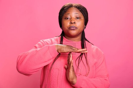 Photo for Angry woman doing timeout gesture with t shape hands making break time sign with arms in studio with pink background. African american young adult advertising pause symbol with palms - Royalty Free Image