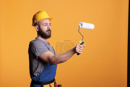 Photo for Professional handyman using rolling brush to do painting job, working on renovating project to color walls. Repairman contractor holding roller paintbrush for redecoration and renovation. - Royalty Free Image