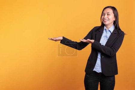 Téléchargez les photos : Femme philippine souriante pointant vers le côté avec index publicité produit de mode tout en se tenant sur fond jaune. Jeune adulte avec une expression faciale positive montrant la promotion - en image libre de droit