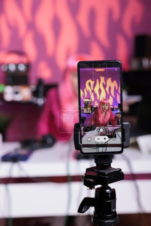 Photo for Influencer filming podcast using mobile phone camera discussing lifestyle advice with subscribers, posting content on her channel. Asian vlogger standing in broadcast studio recording vlog - Royalty Free Image