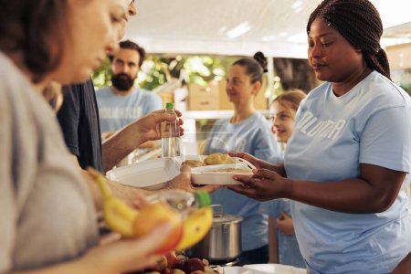 Outdoor-Food-Drive-Veranstaltung mit Freiwilligen verschiedener Ethnien, die Obdachlose betreuen und dabei die Bedeutung der Bekämpfung von Hunger und Armut betonen. Charity-Helfer verteilen kostenlose Lebensmittel an Bedürftige.
