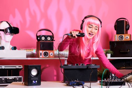 Téléchargez les photos : Musicien asiatique mélangeant chanson techno avec électronique à l'aide d'une console de mixage professionnelle tout en appréciant parler avec les fans, s'amuser ensemble pendant la nuit dans le club. Artiste appréciant jouer de la musique - en image libre de droit