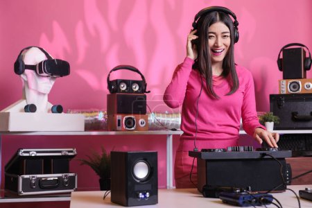 Photo for Cheerful musician standing at dj table mixing electronic music with techno using professional mixer console, having fun in studio over pink background. Artist playing stereo sounds with electronics - Royalty Free Image