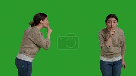 Téléchargez les photos : Femme privée faisant symbole de silence pour garder le silence et le secret sur fond d'écran vert, exprimant la vie privée et le secret sur la caméra. Modèle féminin montrant un geste confidentiel et silencieux, faisant signe shh. - en image libre de droit