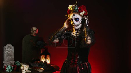 Photo for Female model listening to music on audio headset, using headphones to enjoy mp3 song over black background. Creepy horror woman using headphones on holy dios de los muertos tradition. - Royalty Free Image