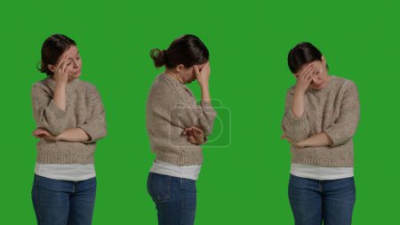 Photo for Close up of adult dealing with painful headache on camera, rubbing temples to cure sickness. Person suffering from migraine over isolated green screen backdrop, unwell ill woman in studio. - Royalty Free Image