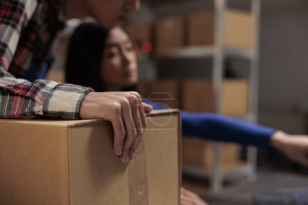 Photo for Postal service wroker holding cardboard box while managing inventory with coworker in warehouse. Storehouse employees packing and dispatching parcel with customer order close up - Royalty Free Image