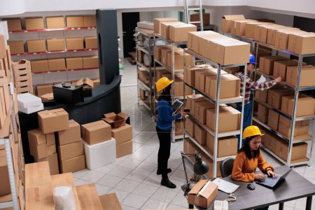 Warehouse employees team working in order fulfillment center. Asian man and women storehouse workers scanning parcels, searching packages and doing inventory on laptop top view