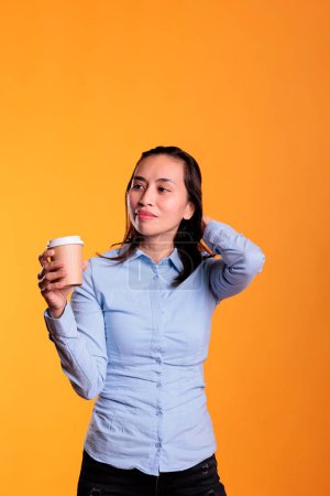 Foto de Mujer filipina posando en el estudio con una taza de café, disfrutando de una bebida caliente sobre un fondo amarillo. Positivo adulto sosteniendo papercup usando bebida para tener energía y refresco. - Imagen libre de derechos