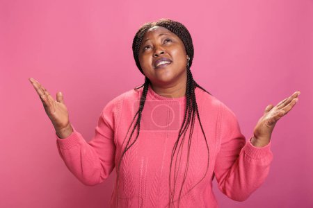 Photo for Faithful catholic woman in pink sweather standing with palms faced to sky pleading and begging to forgiveness. Religious african american young adult praying for a better life over pink background - Royalty Free Image